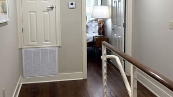 A hallway with a wooden floor, a white door with a vent, and a staircase with a handrail.
