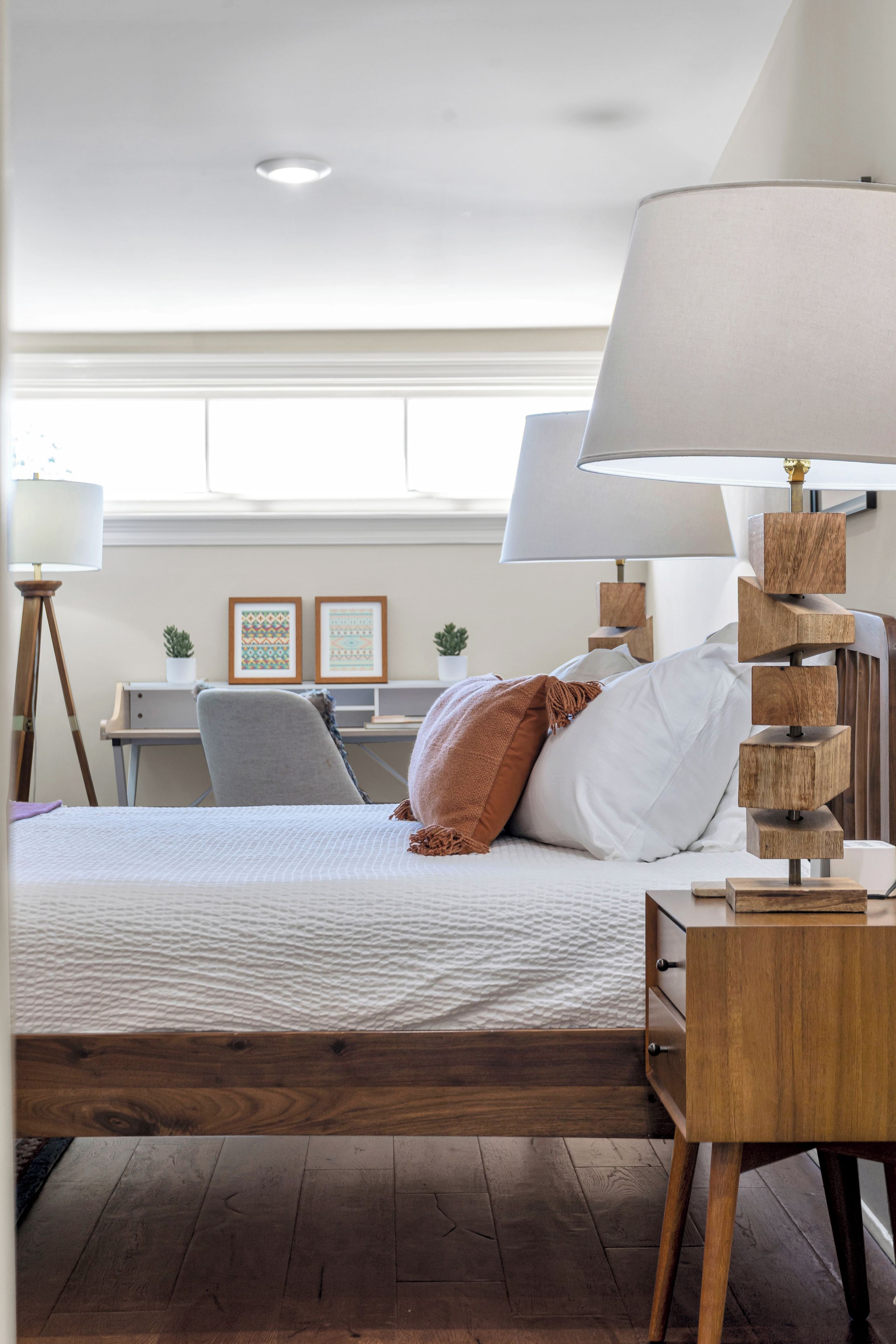 A bedroom with a bed, bedside lamps, a desk, and a window.