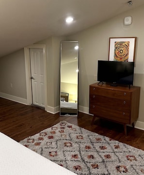 Een kamer met een houten dressoir, een flatscreen televisie, een grote spiegel en een kamerkleed met een patroon.