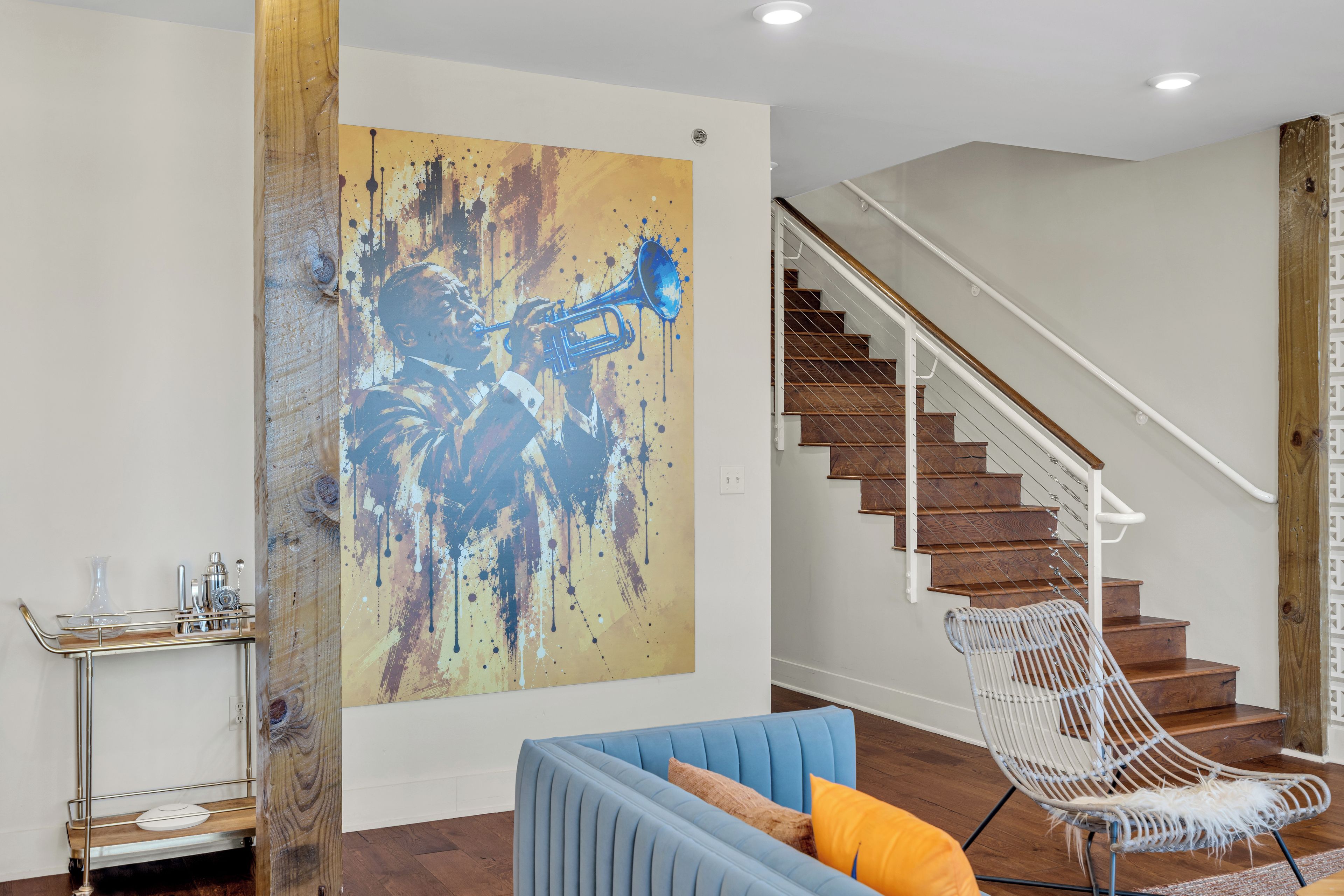 A living room with a blue sofa, a white chair, a large abstract painting, and a staircase.