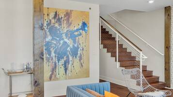 A living room with a blue sofa, a white chair, a large abstract painting, and a staircase.