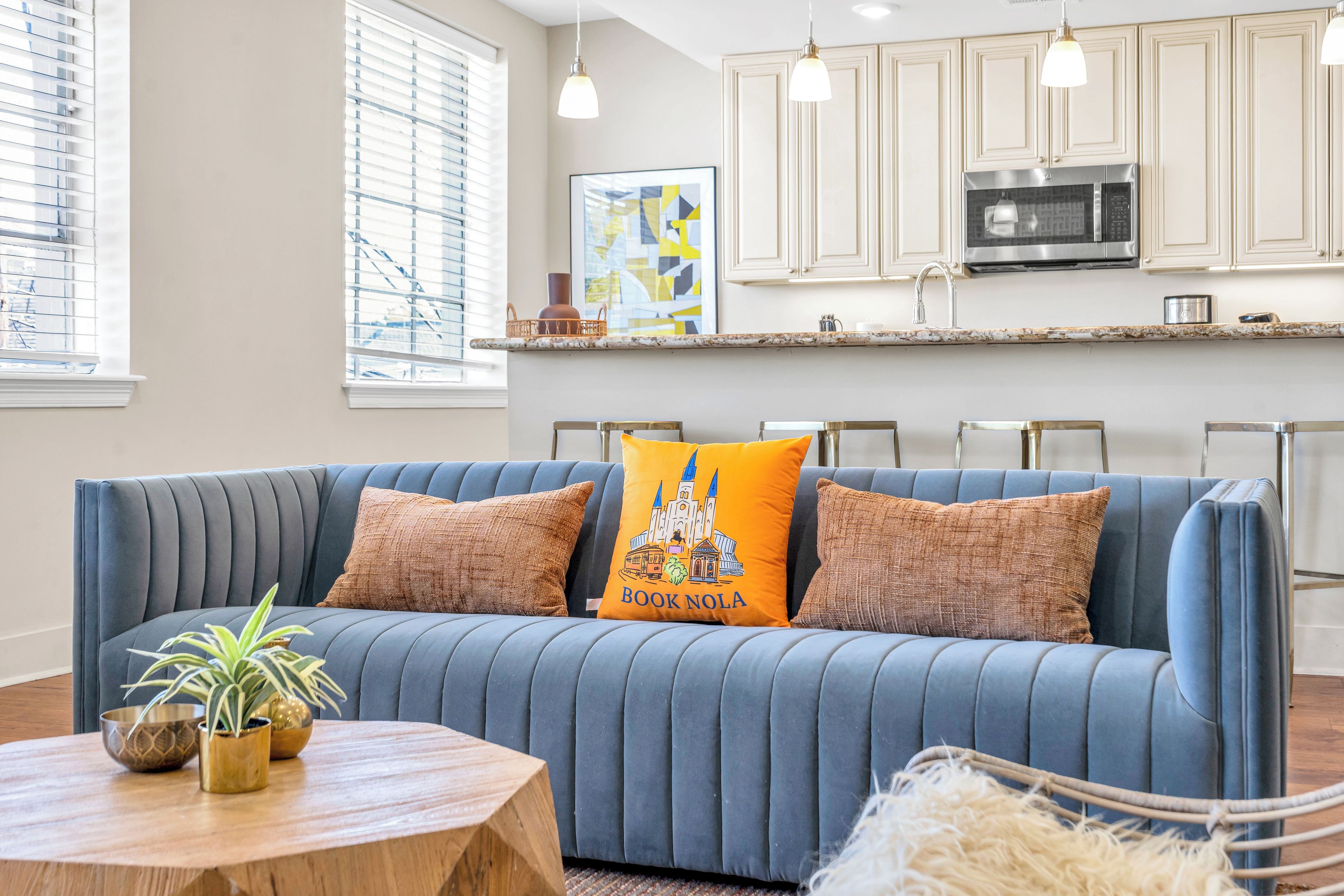 A modern living room with a blue sofa, a wooden coffee table, and a kitchen in the background.