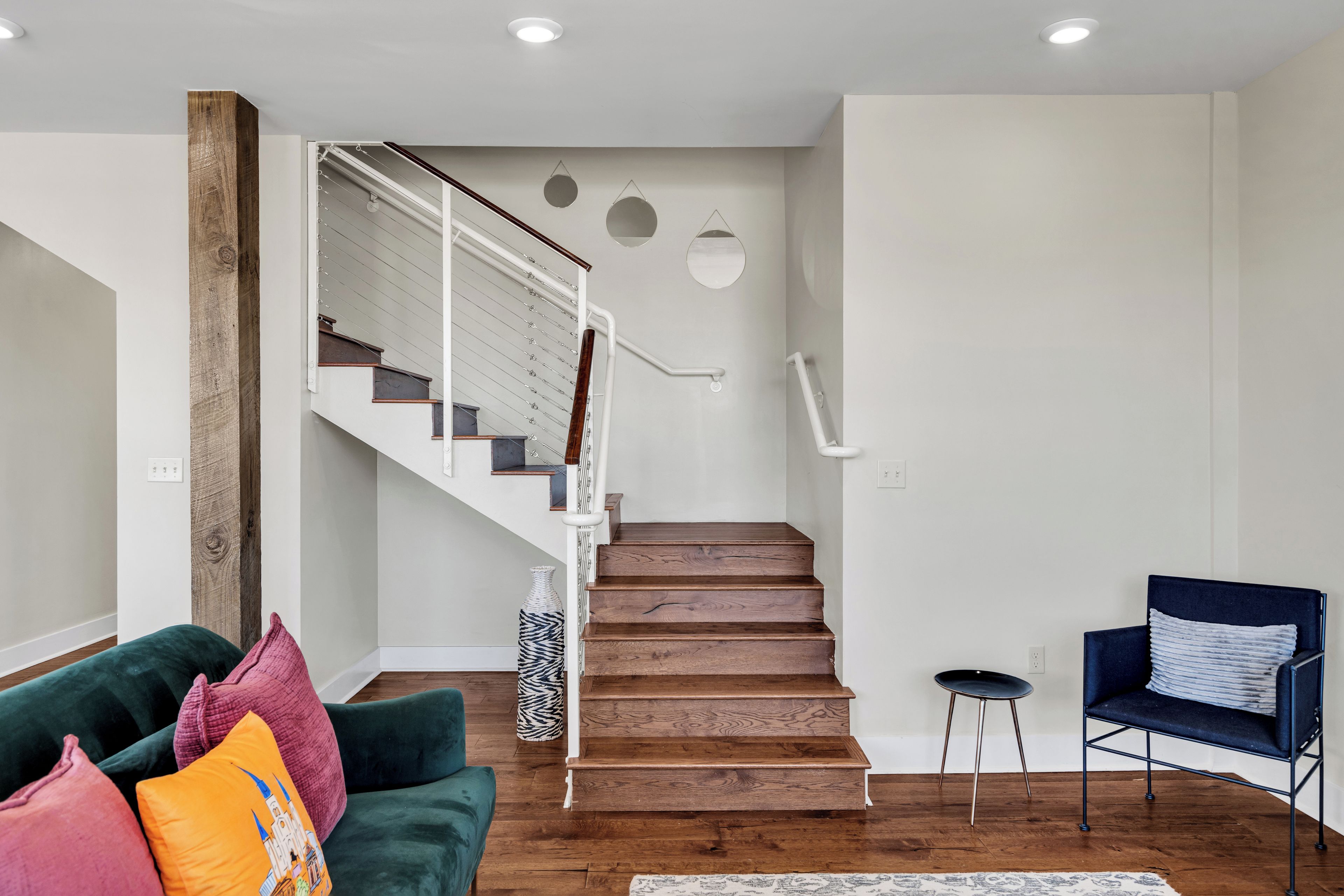 A modern interior with a wooden staircase, a green sofa with colorful cushions, and a blue chair.