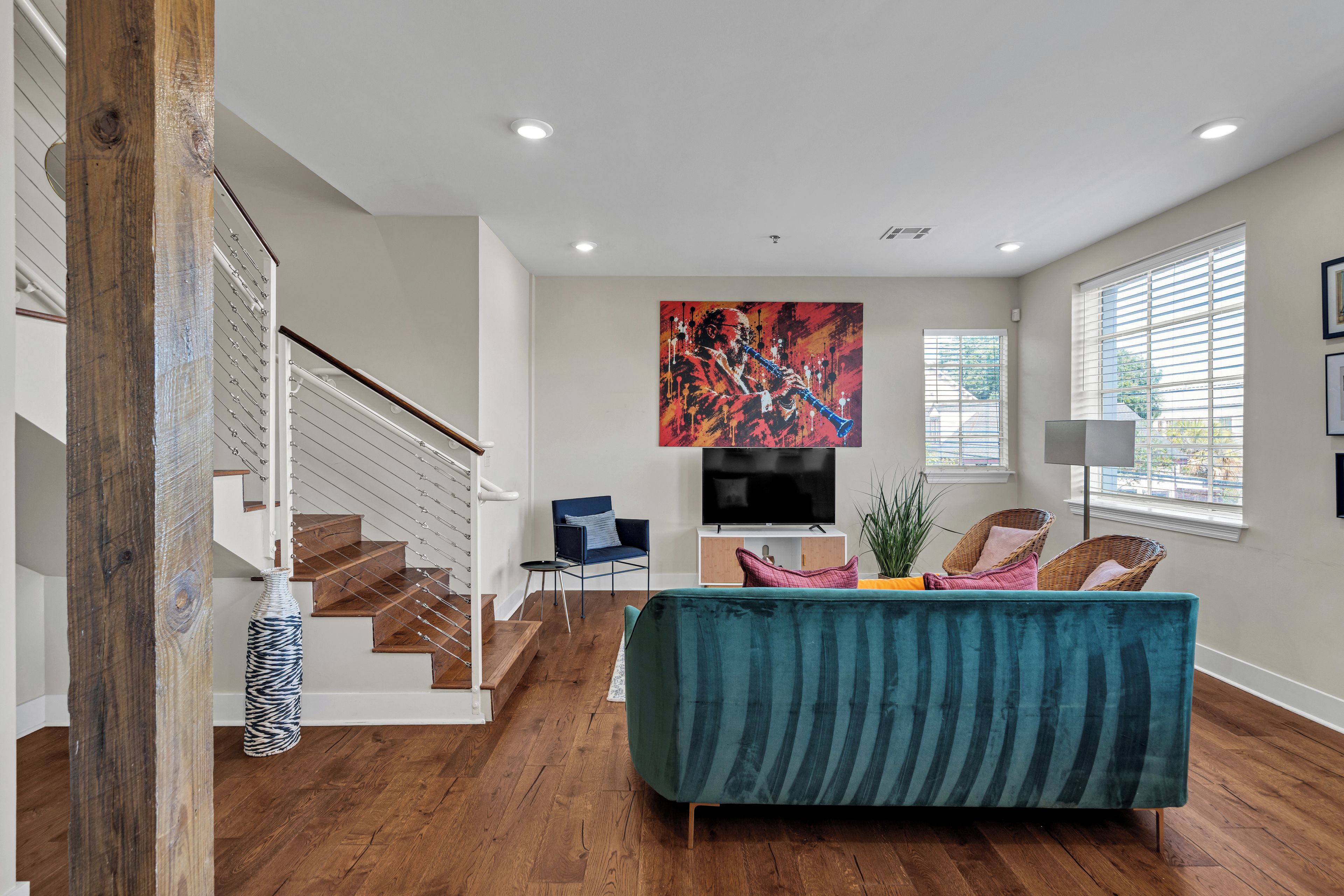 A modern living room with a staircase, a flat-screen TV, and a large abstract painting.