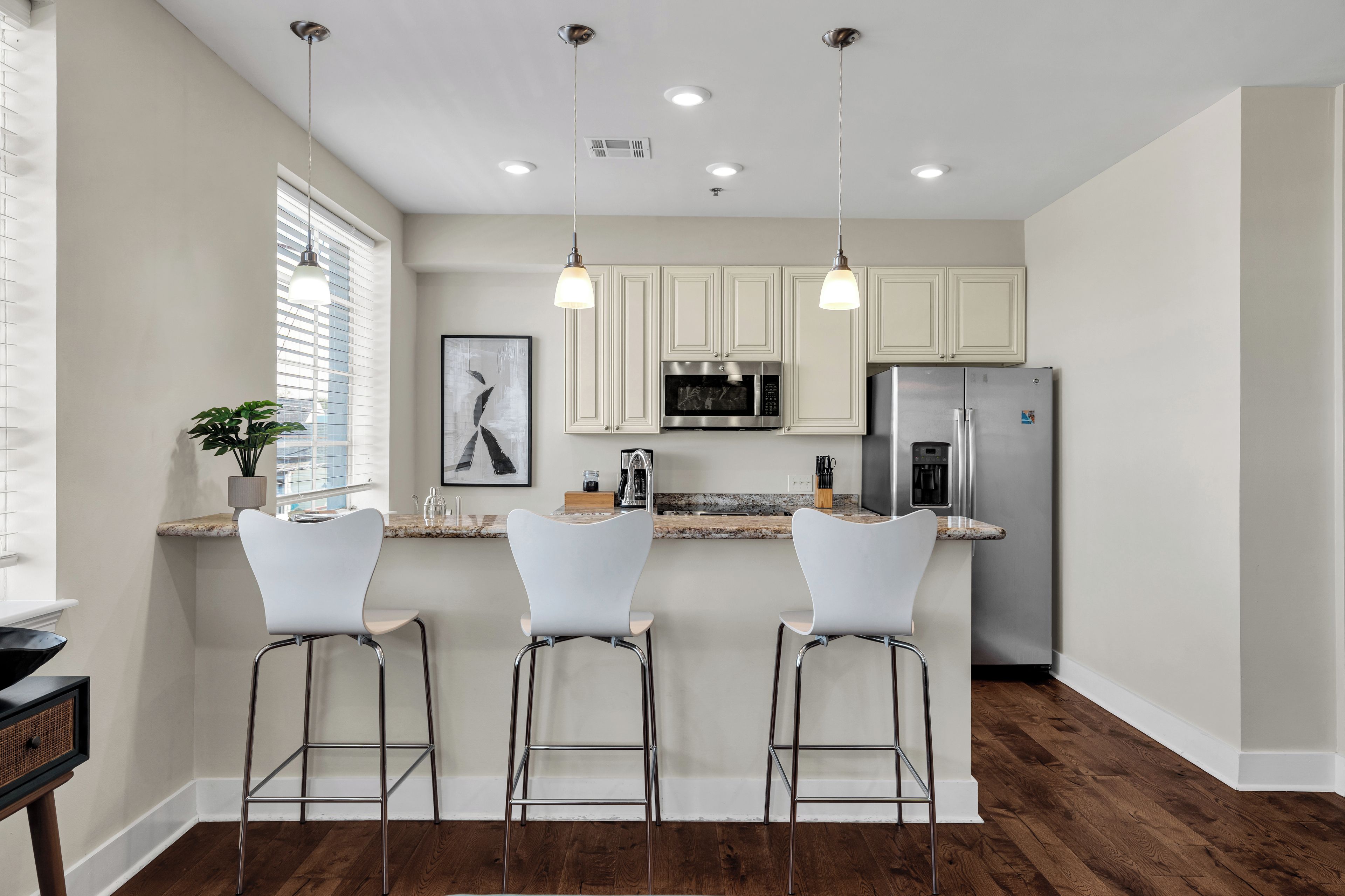 A modern kitchen with white cabinets, stainless steel appliances, and three white bar stools.