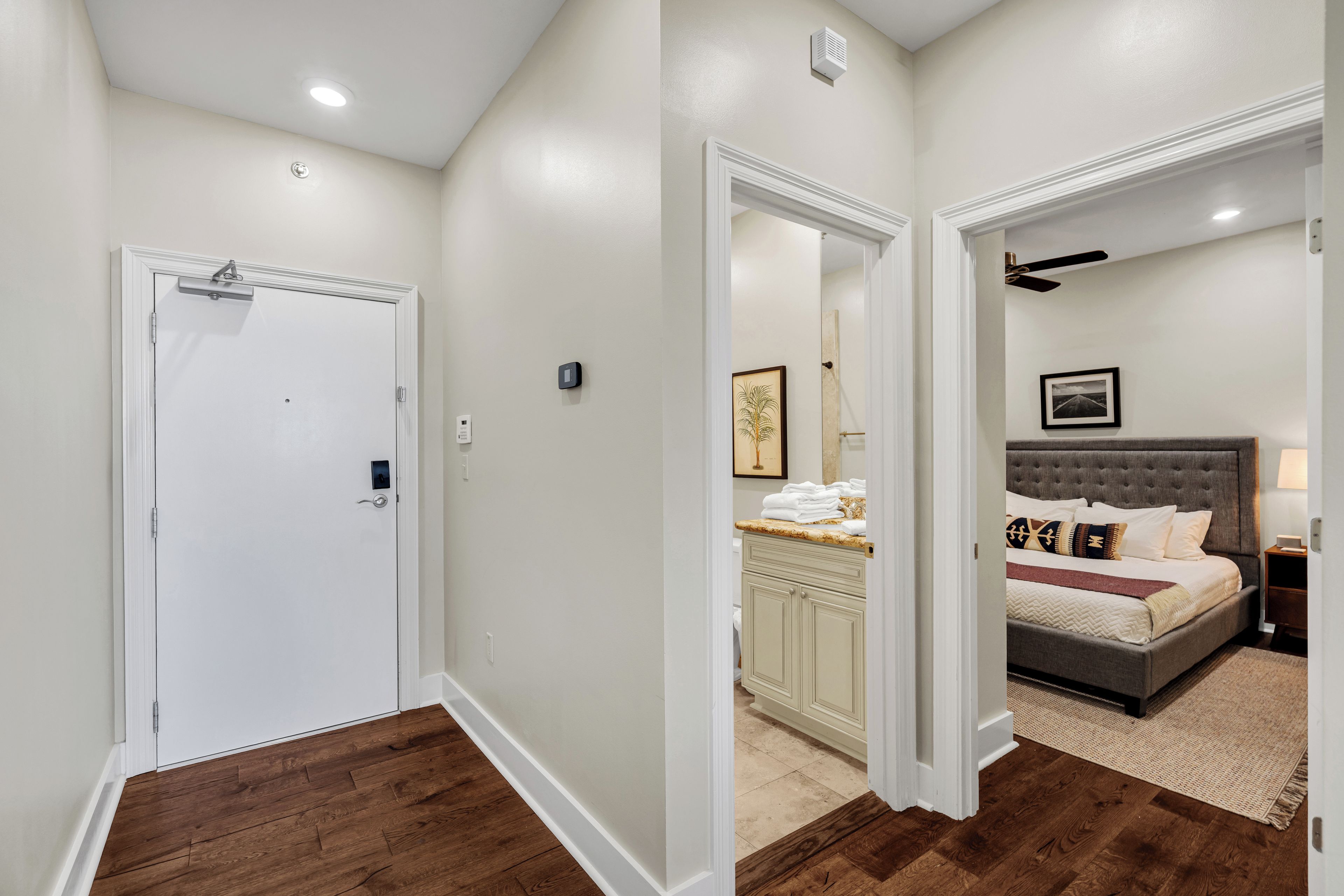 A hallway leading to a bedroom with a bed, a nightstand, and a ceiling fan.