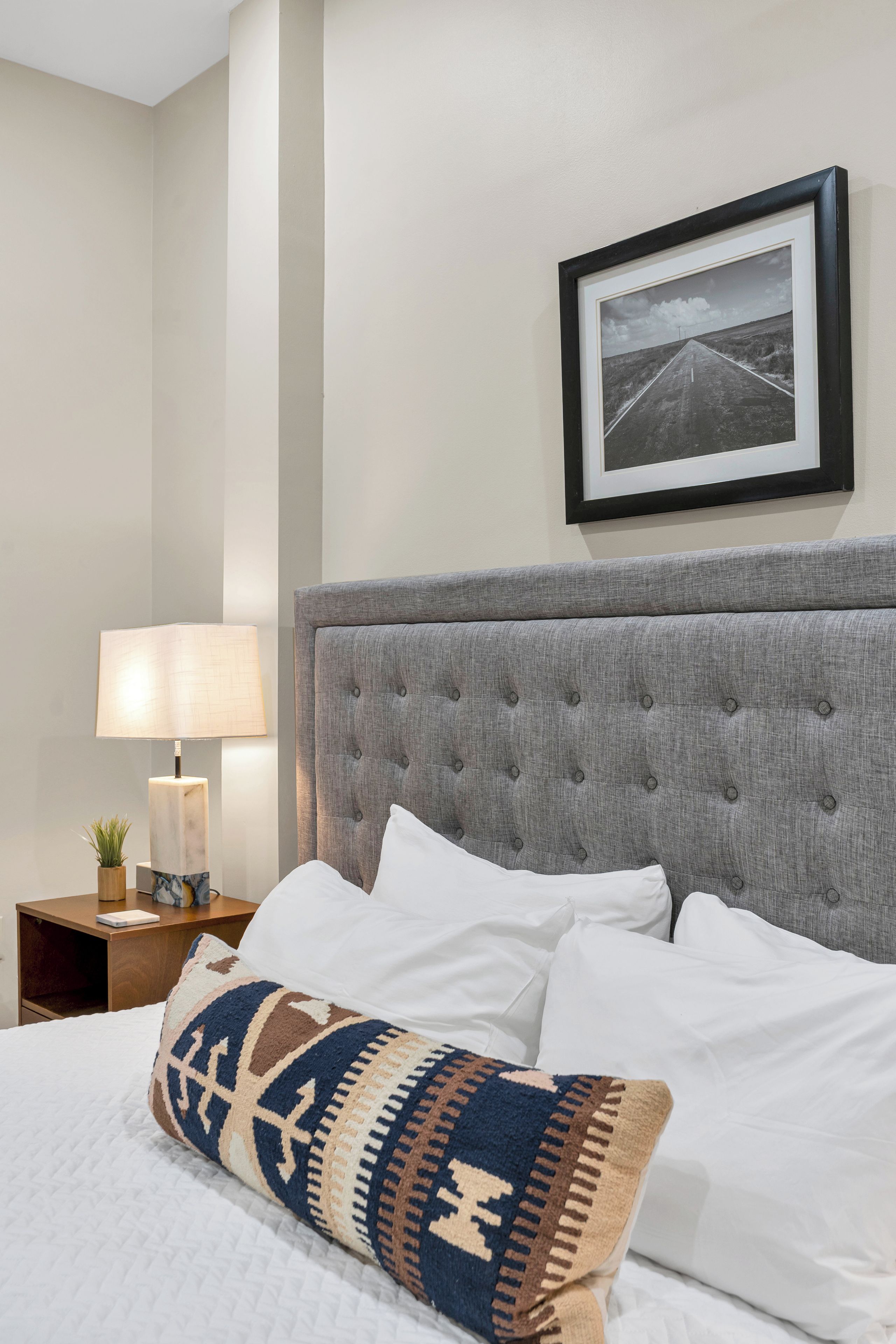 A hotel room with a bed, a nightstand, a lamp, and a framed picture on the wall.