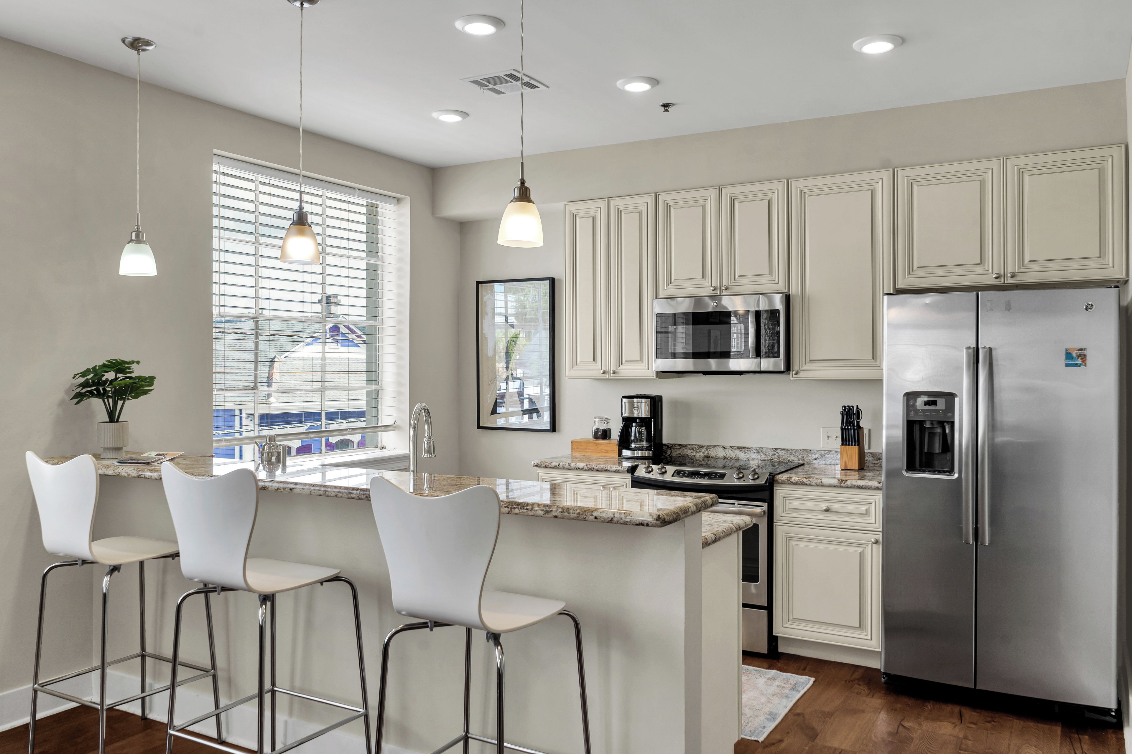 A modern kitchen with a central island, bar stools, stainless steel appliances, and a view through the window.
