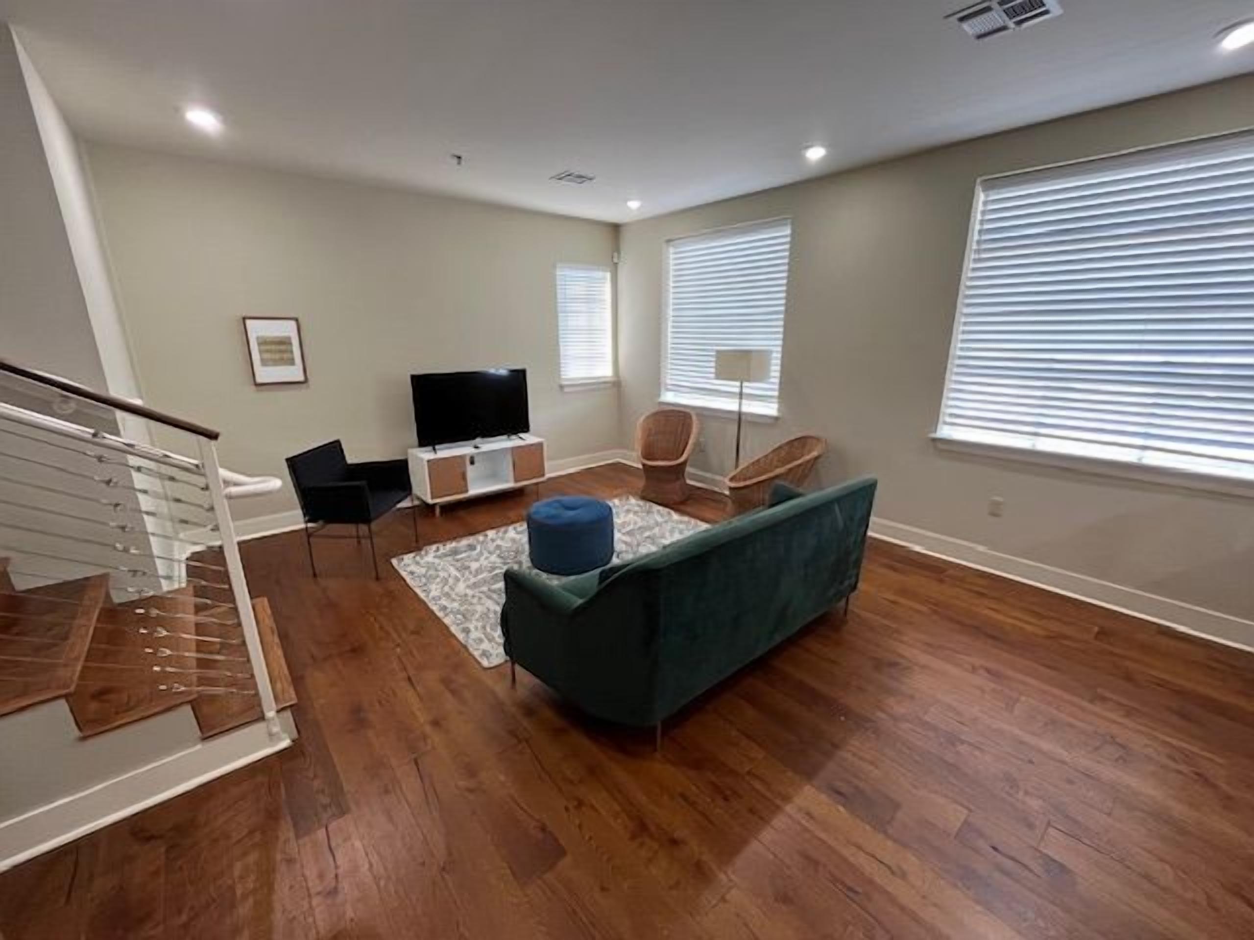 A spacious living room with hardwood flooring, a green sofa, a flat-screen TV, and a staircase.