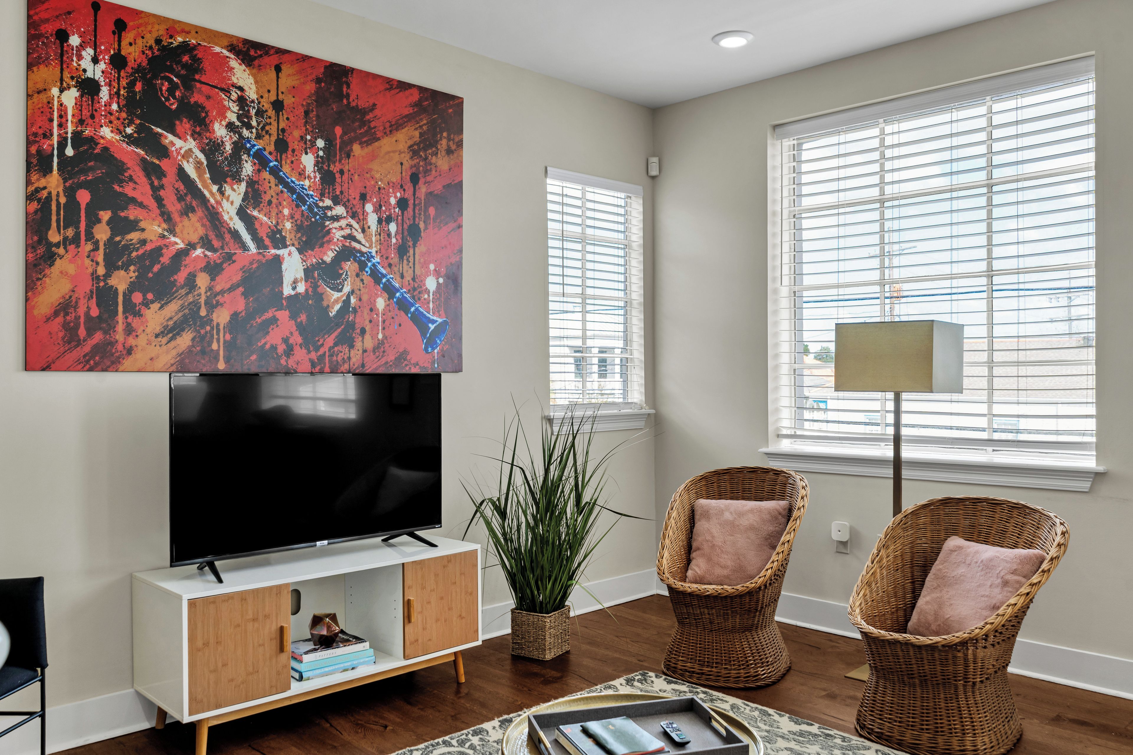 A modern living room with a flat-screen TV, two wicker chairs, a large abstract painting, and a floor lamp.