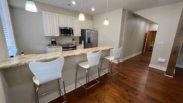 A modern kitchen with a bar area, white bar stools, and stainless steel appliances.