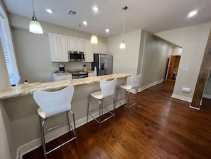 A modern kitchen with a bar area, white bar stools, and stainless steel appliances. - Stylish 2BR condo near Frenchmen St (New Orleans)