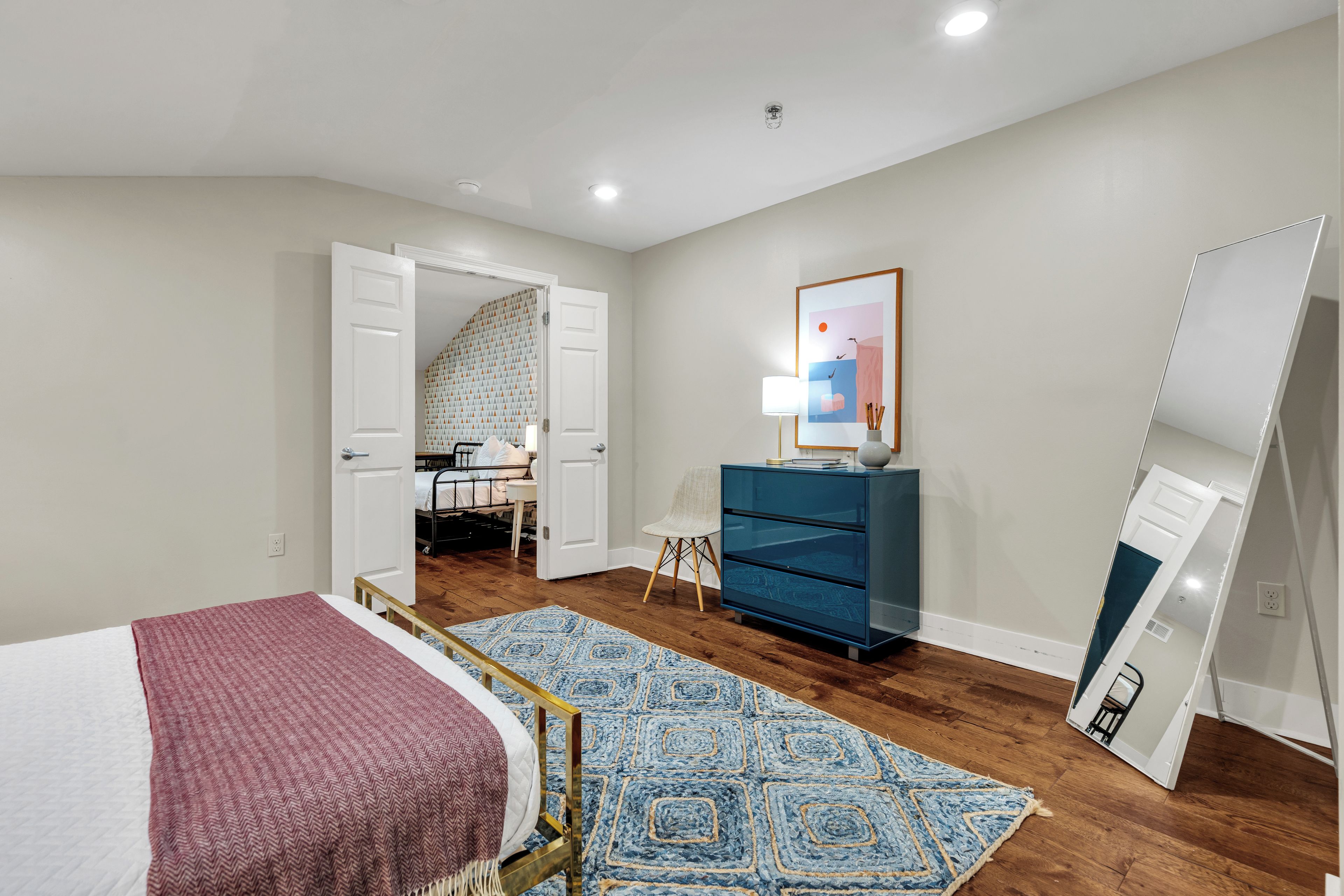A bedroom with a bed, a desk, a chair, a dresser, and a mirror.