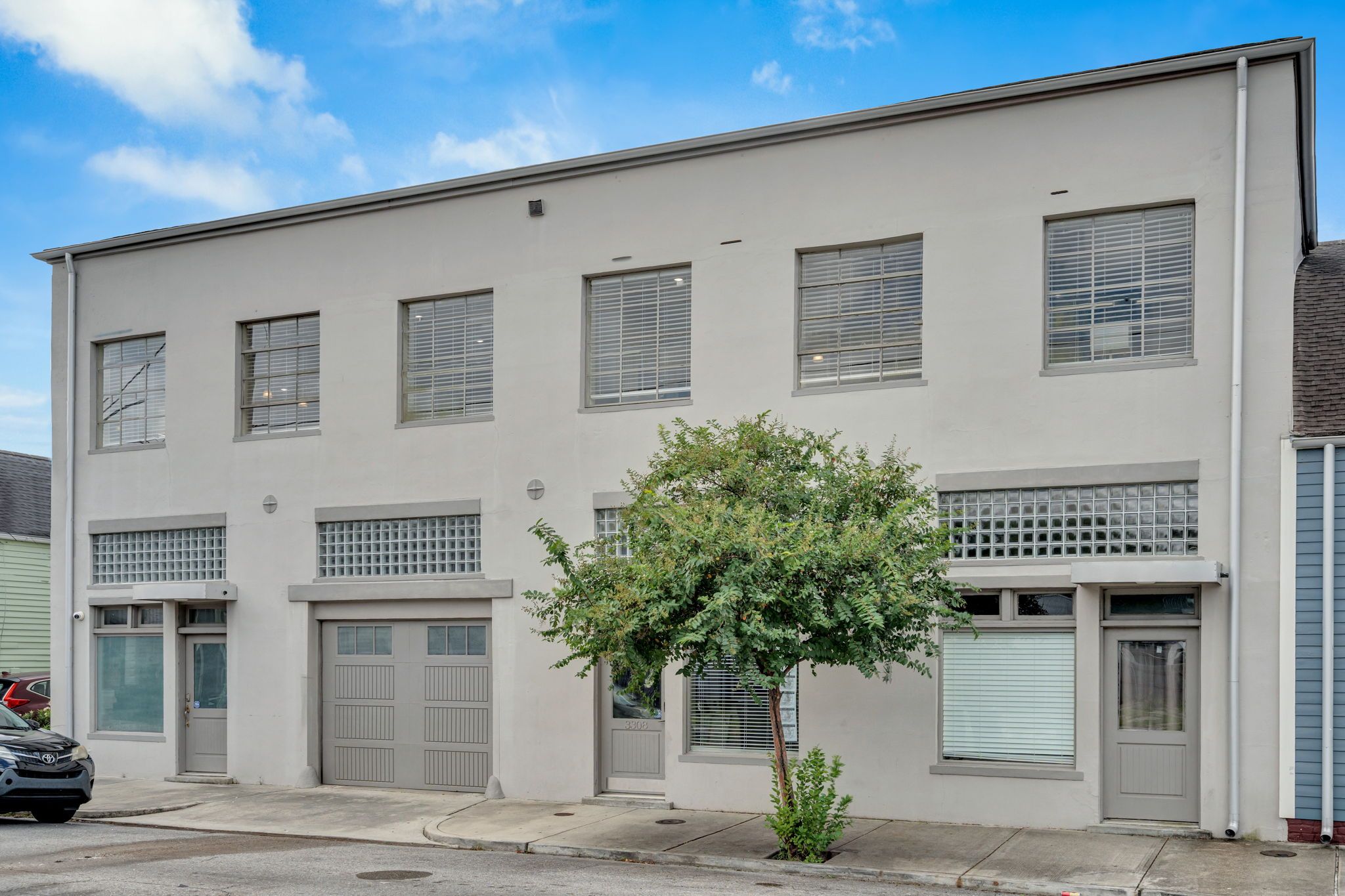 A two-story building with a garage door, a small tree in front, and a clear blue sky.