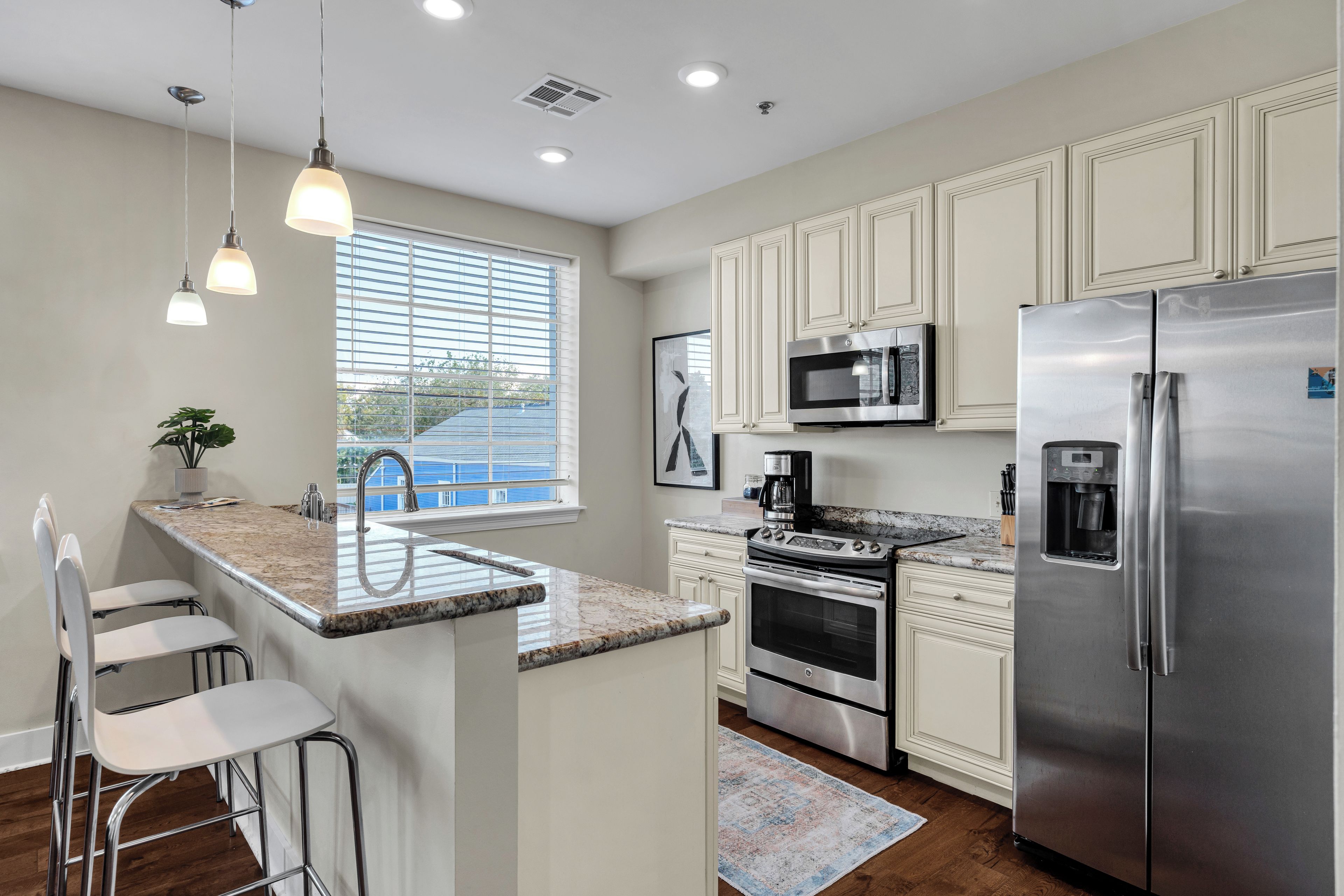 A modern kitchen with white cabinets, stainless steel appliances, a granite countertop, and a window with blinds.