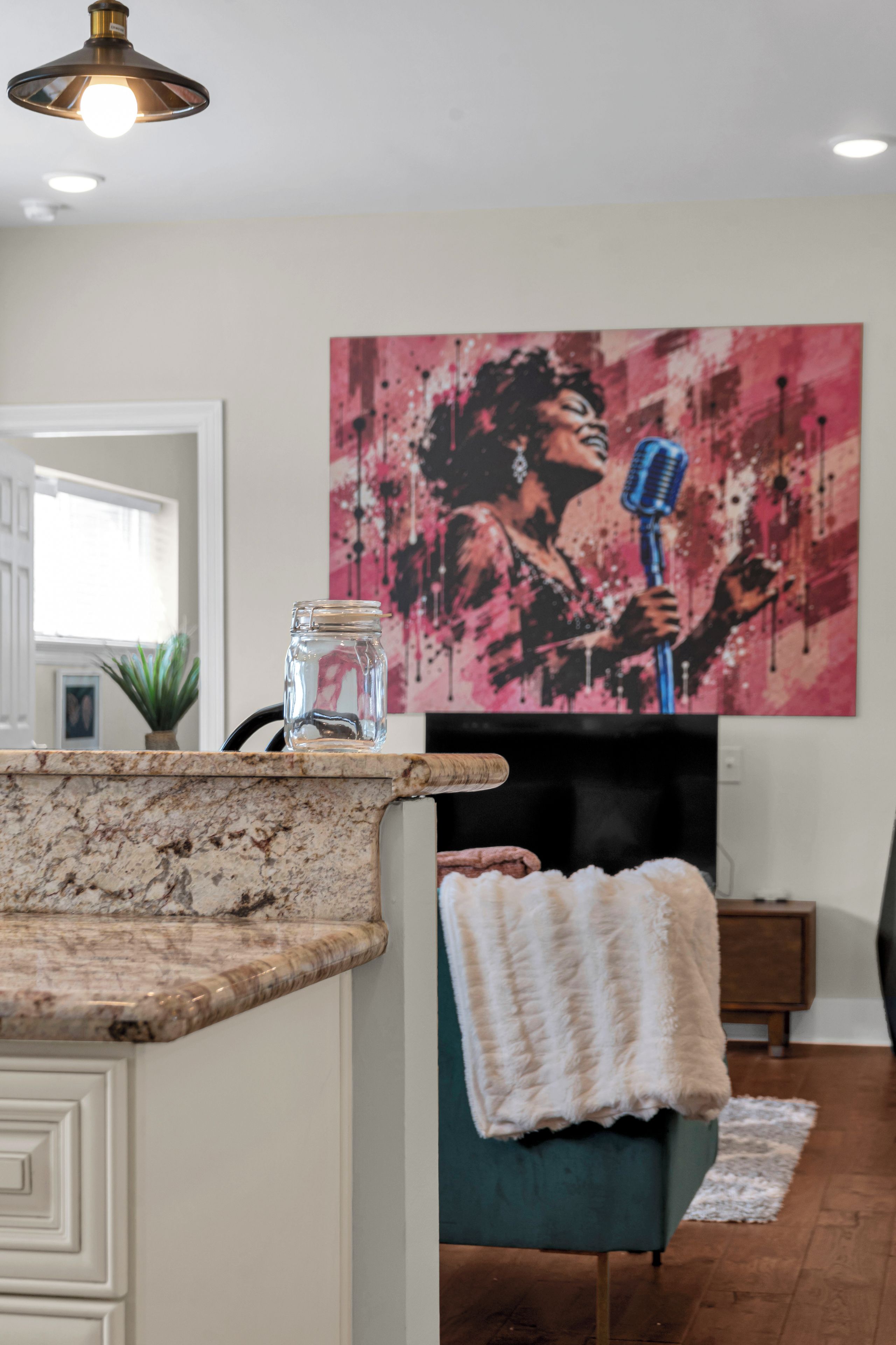 A modern kitchen with a marble countertop, a clear glass jar, and a green upholstered chair.
