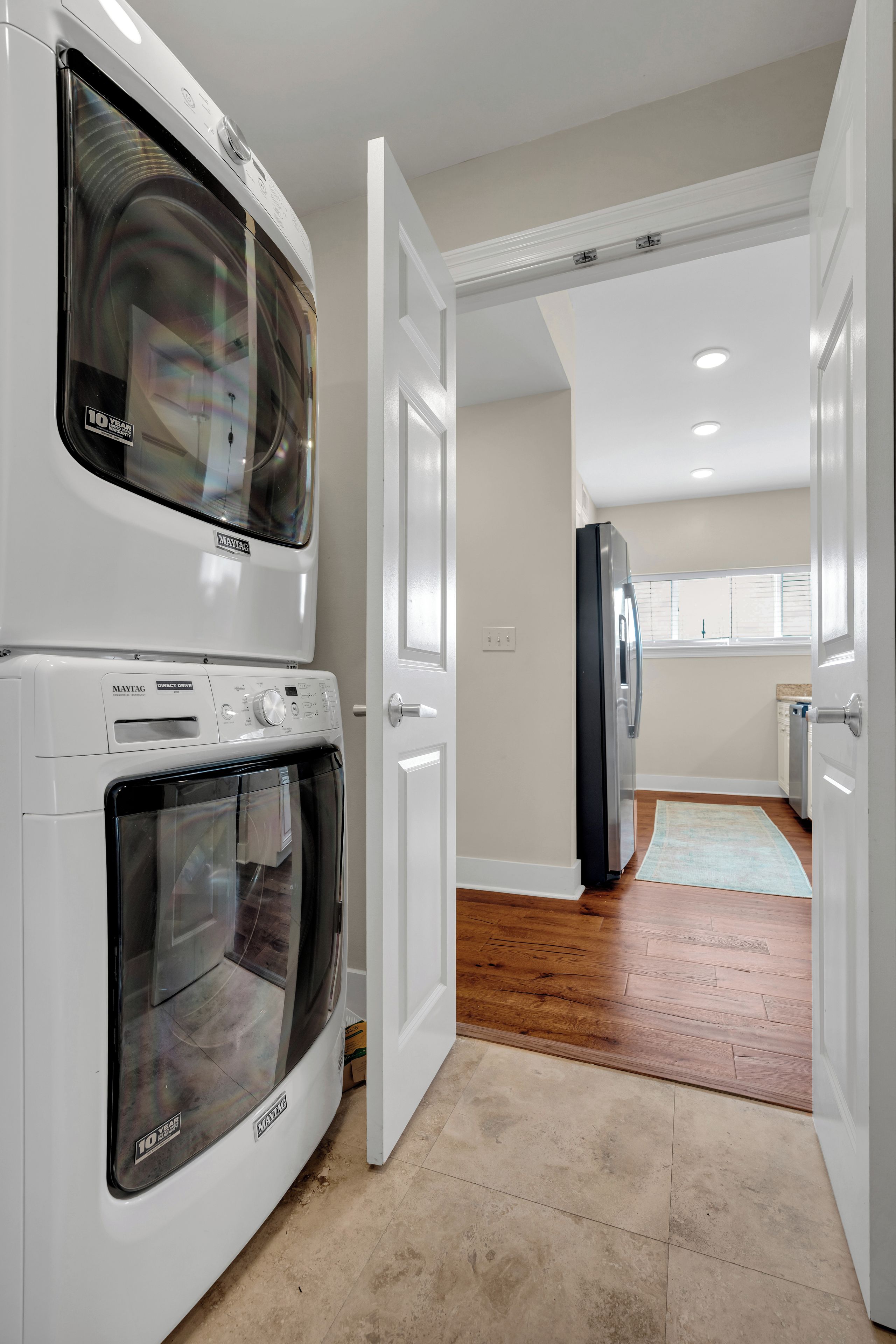 A laundry room with a Maytag washer and dryer, a refrigerator, and a wooden floor.