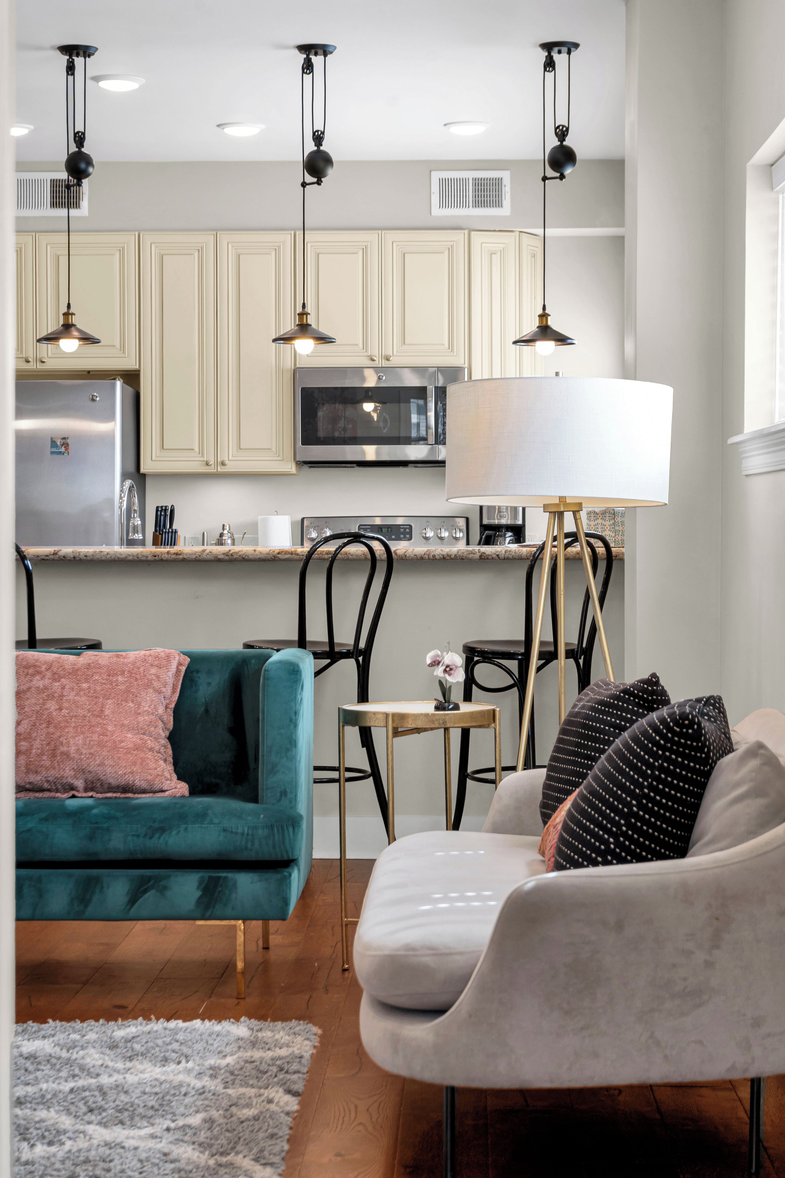 A modern kitchen with a built-in microwave, a stainless steel refrigerator, and a dining area with a teal sofa and a grey armchair.