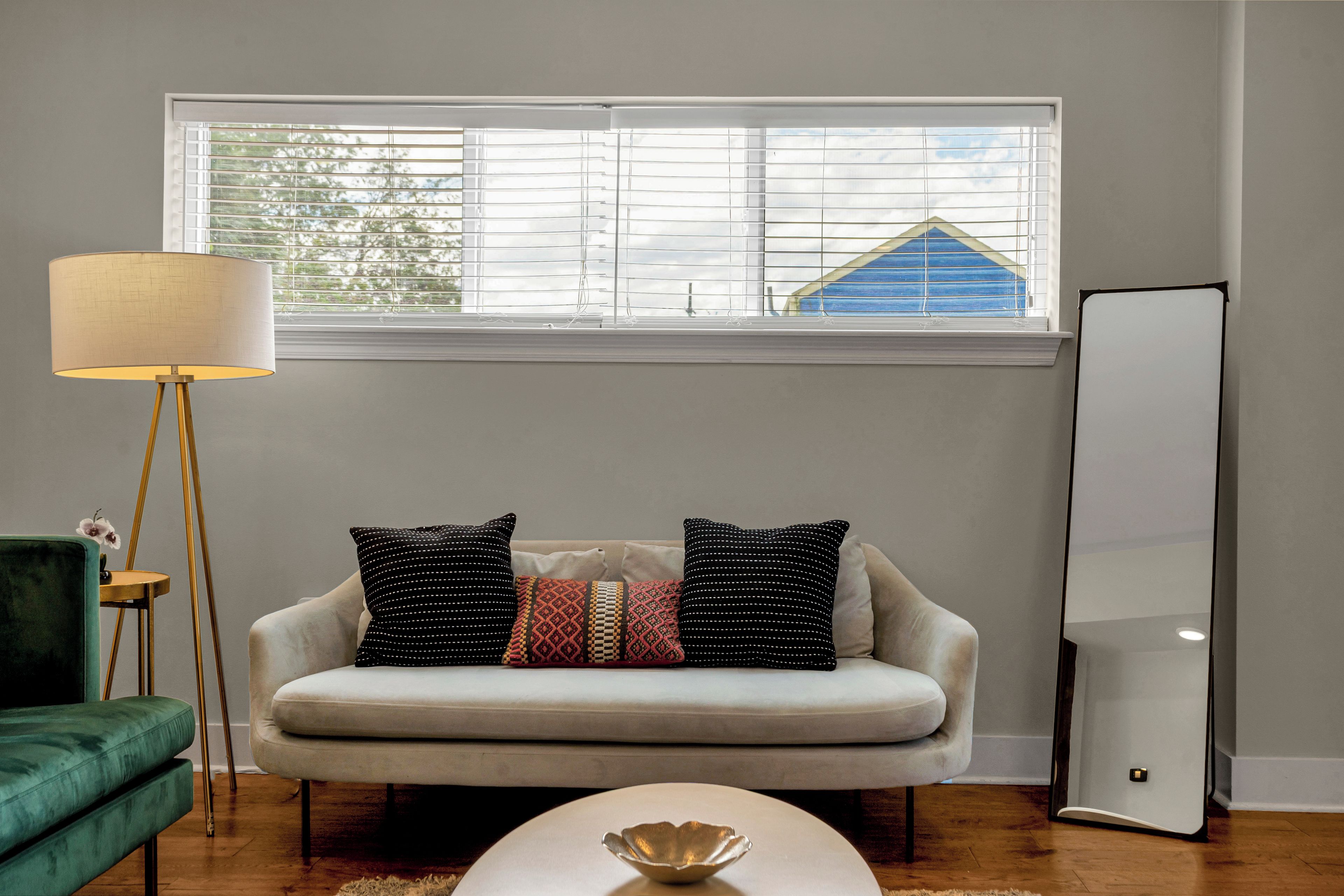 A living room with a sofa, a floor lamp, a round table, and a large mirror.