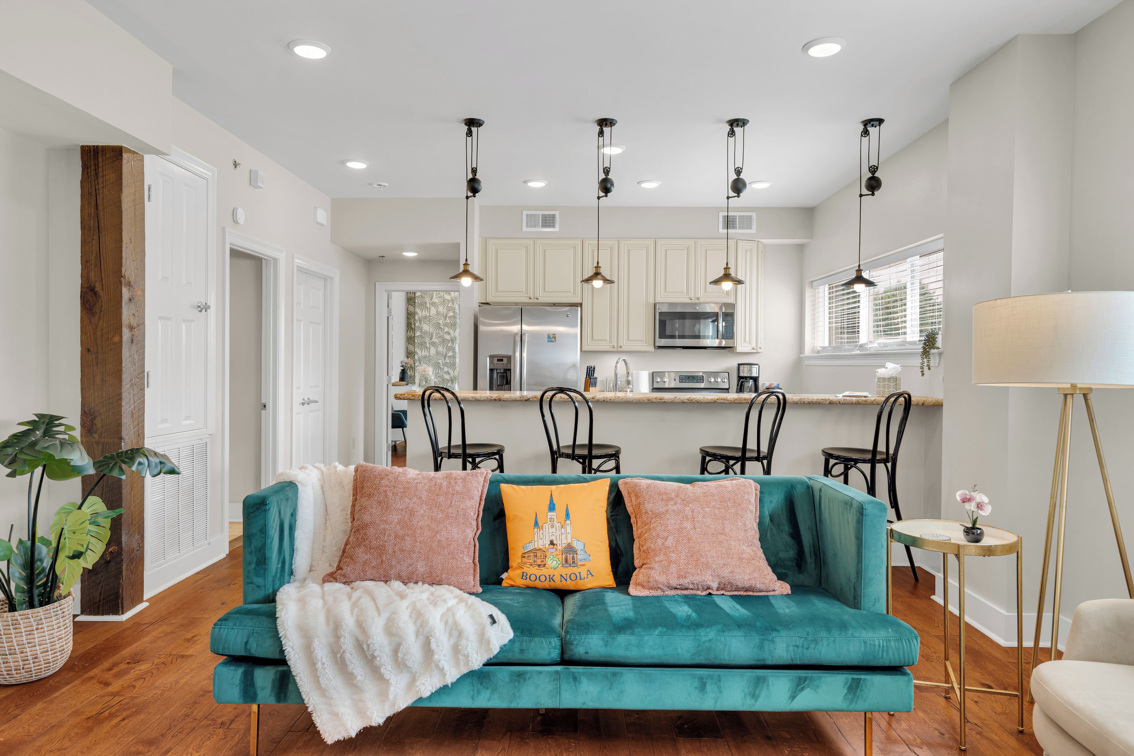 A modern living room with a teal sofa, a white throw blanket, and decorative pillows.