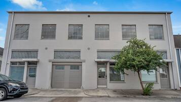 A two-story building with a garage door, a small tree in front, and a parked car.