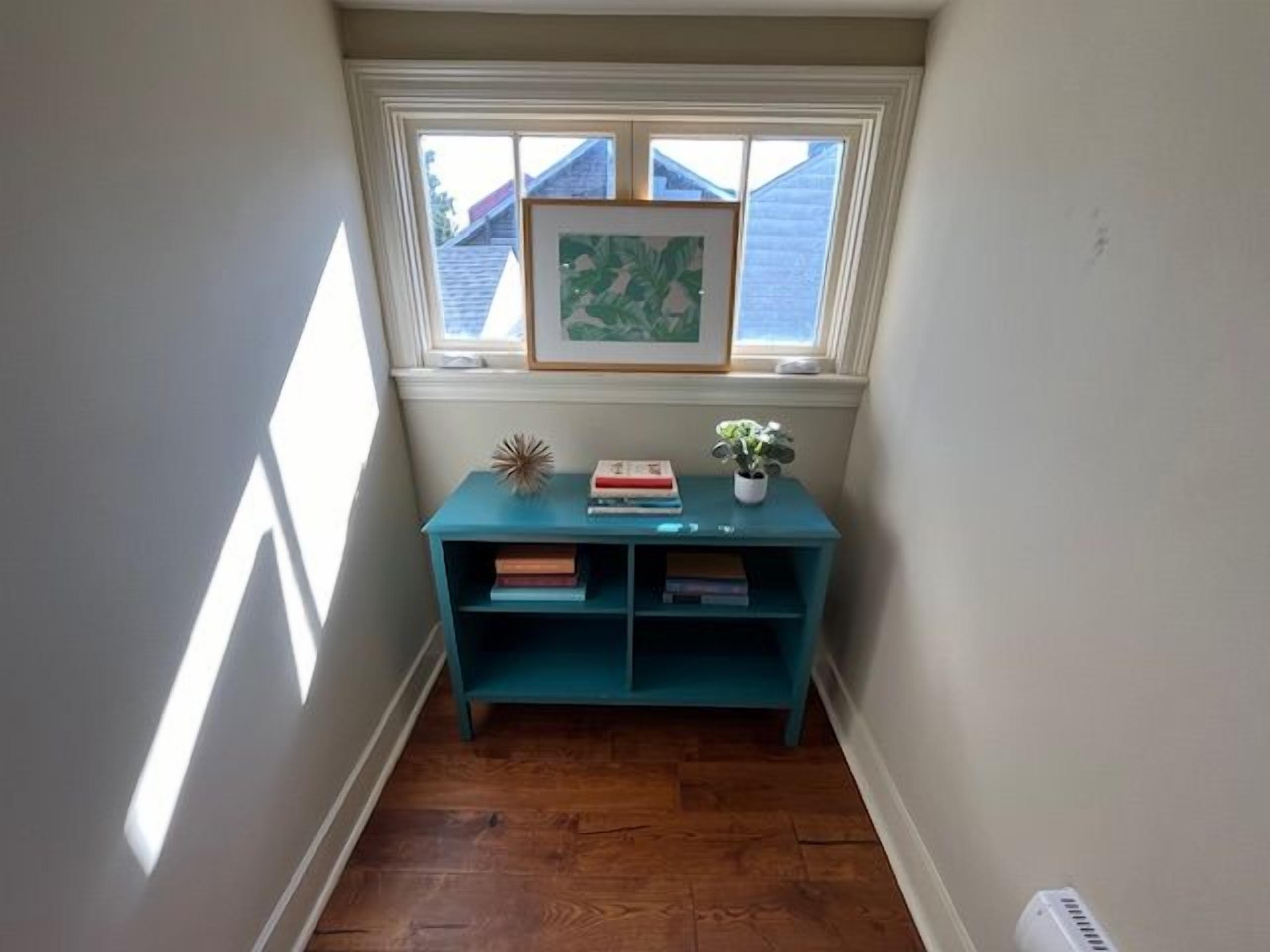 A corner room with a window, a teal bookshelf, and a small plant.
