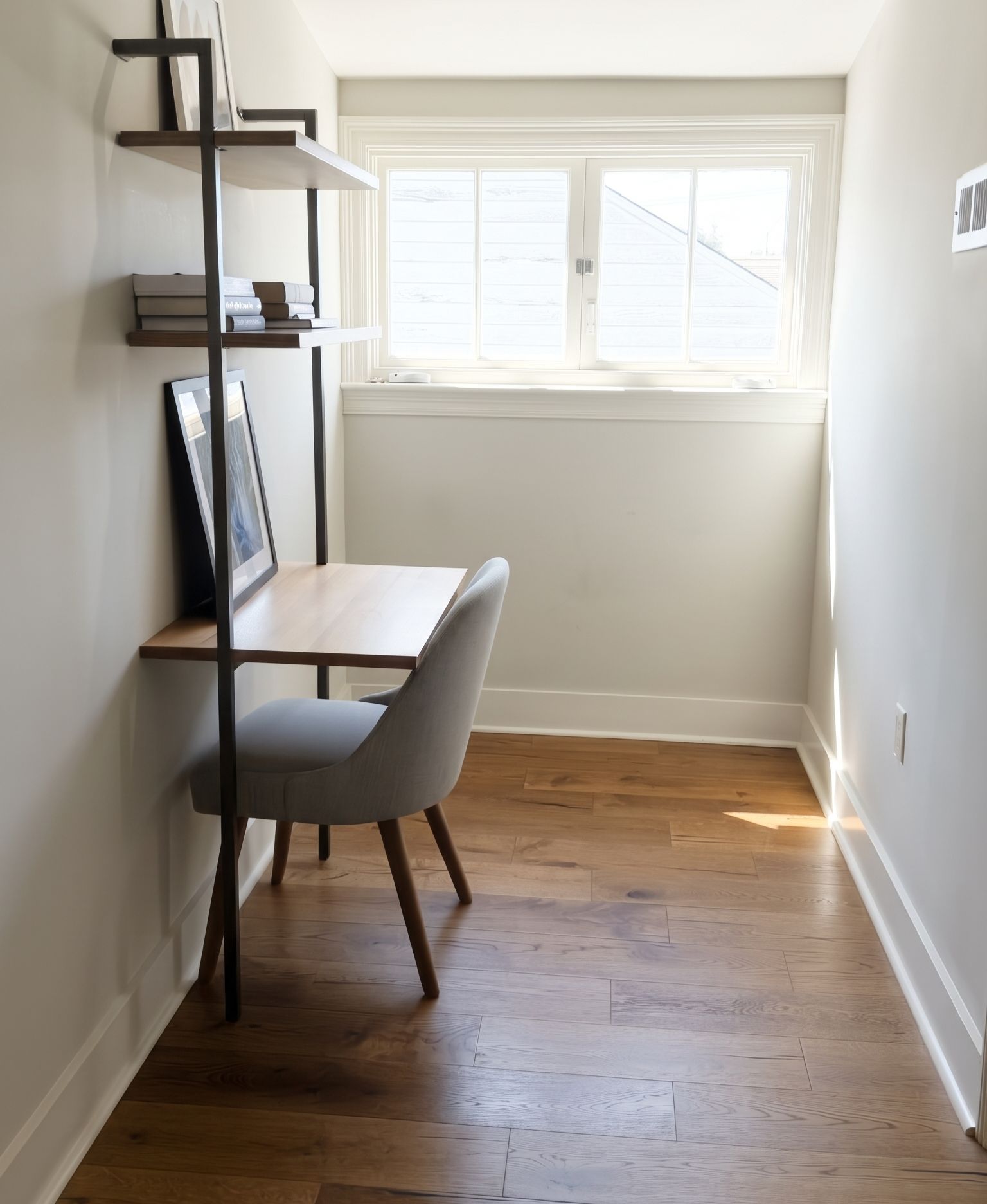 A small, bright room with a wooden floor, a desk, a chair, and a window with blinds.