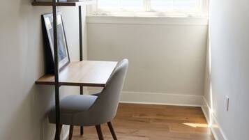 A small, bright room with a wooden floor, a desk, a chair, and a window with blinds.