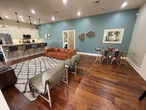 A modern living room with a sofa, a glass dining table, and a kitchen area with white cabinets and a microwave. - Comfortable 2BR New Orleans vacation rental in Bywater, sleeping 4 with 2 queen beds. Located at historic Burgundy & Piety, steps from Crescent Park and a short ride to Frenchmen Street & the French Quarter. (New Orleans)