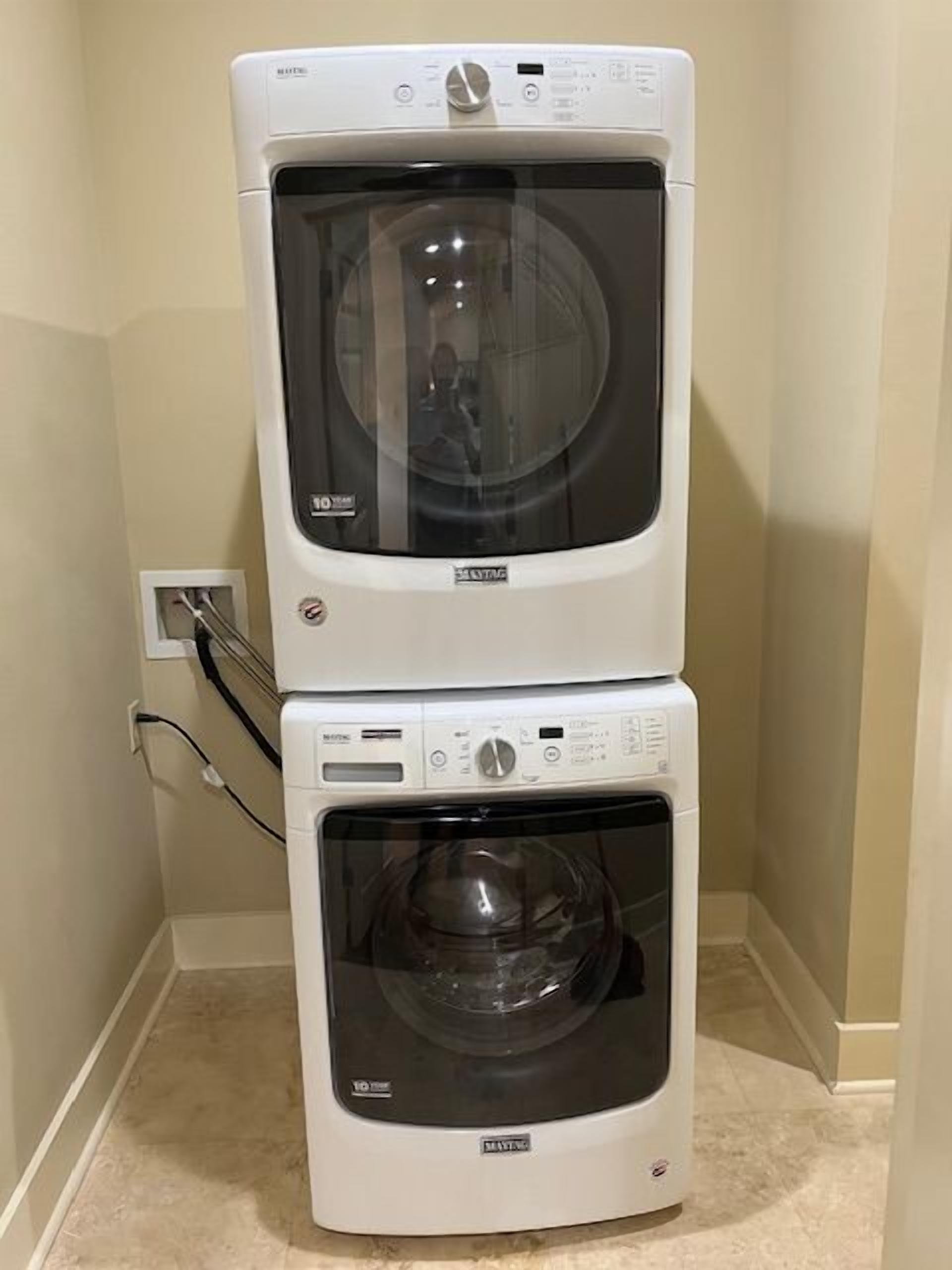 A stacked washer and dryer unit in a corner with a visible power outlet.