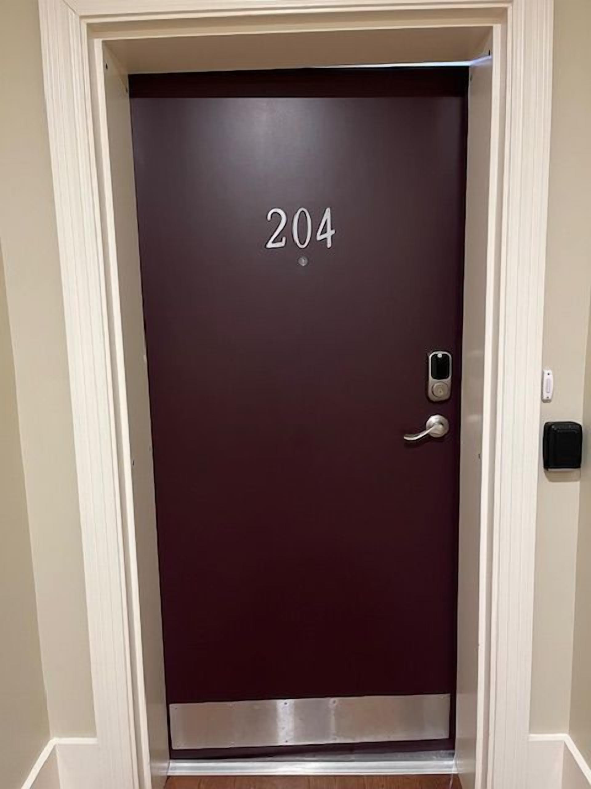 A dark-colored door with the number 204, a door handle, and a small electronic lock.