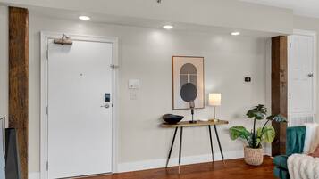 A room with a white door, a small table with a bowl and a lamp, a framed picture on the wall, and a green chair with a white throw.