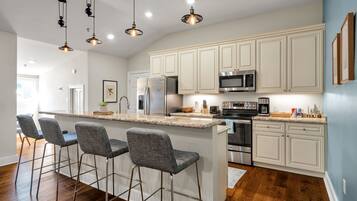 A modern kitchen with bar stools, stainless steel appliances, and pendant lighting.