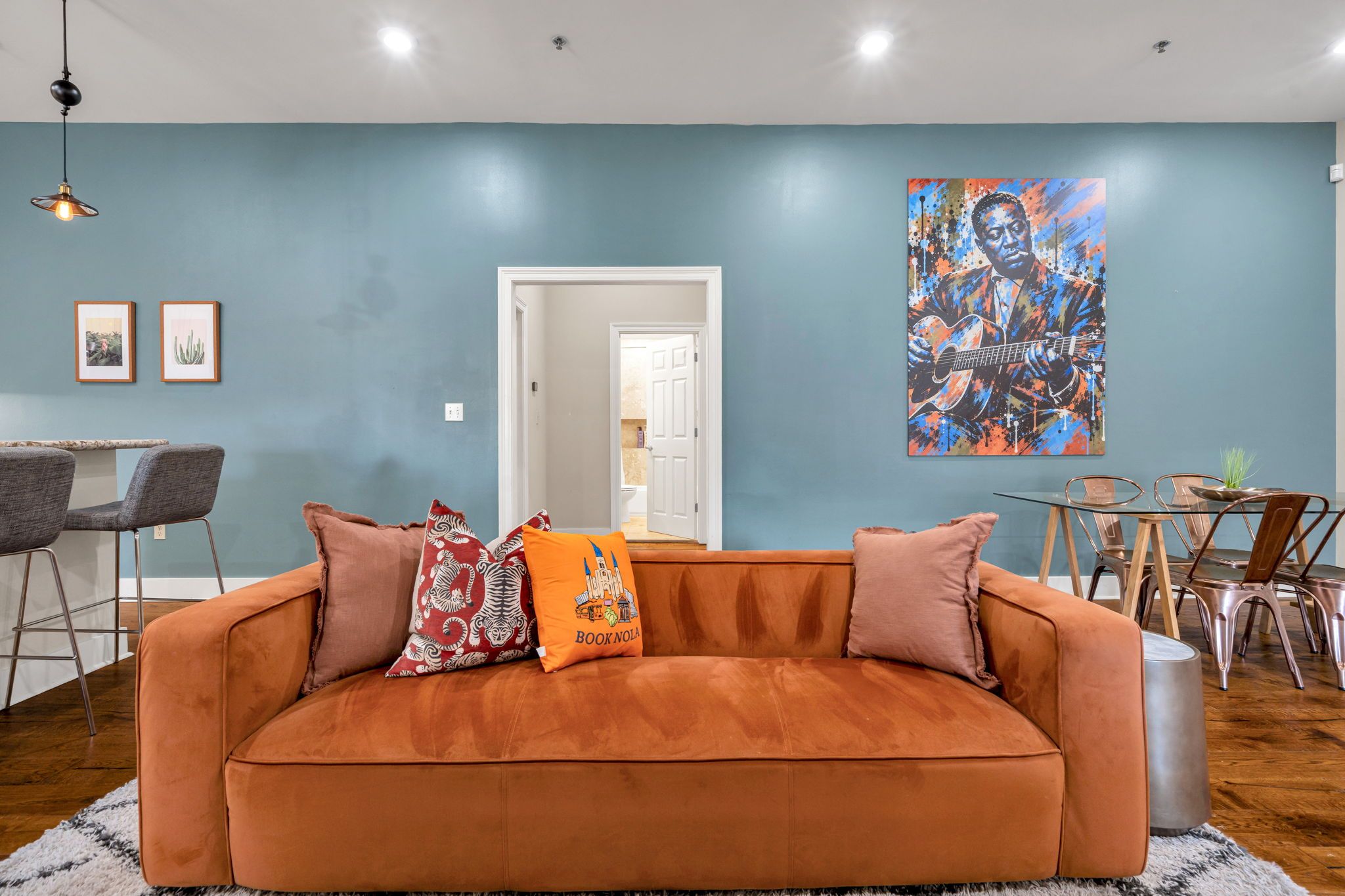 Ein Wohnzimmer mit einer Couch, einem Esstisch mit Stühlen, einem Gemälde an der Wand und einer Tür zu einem anderen Raum.