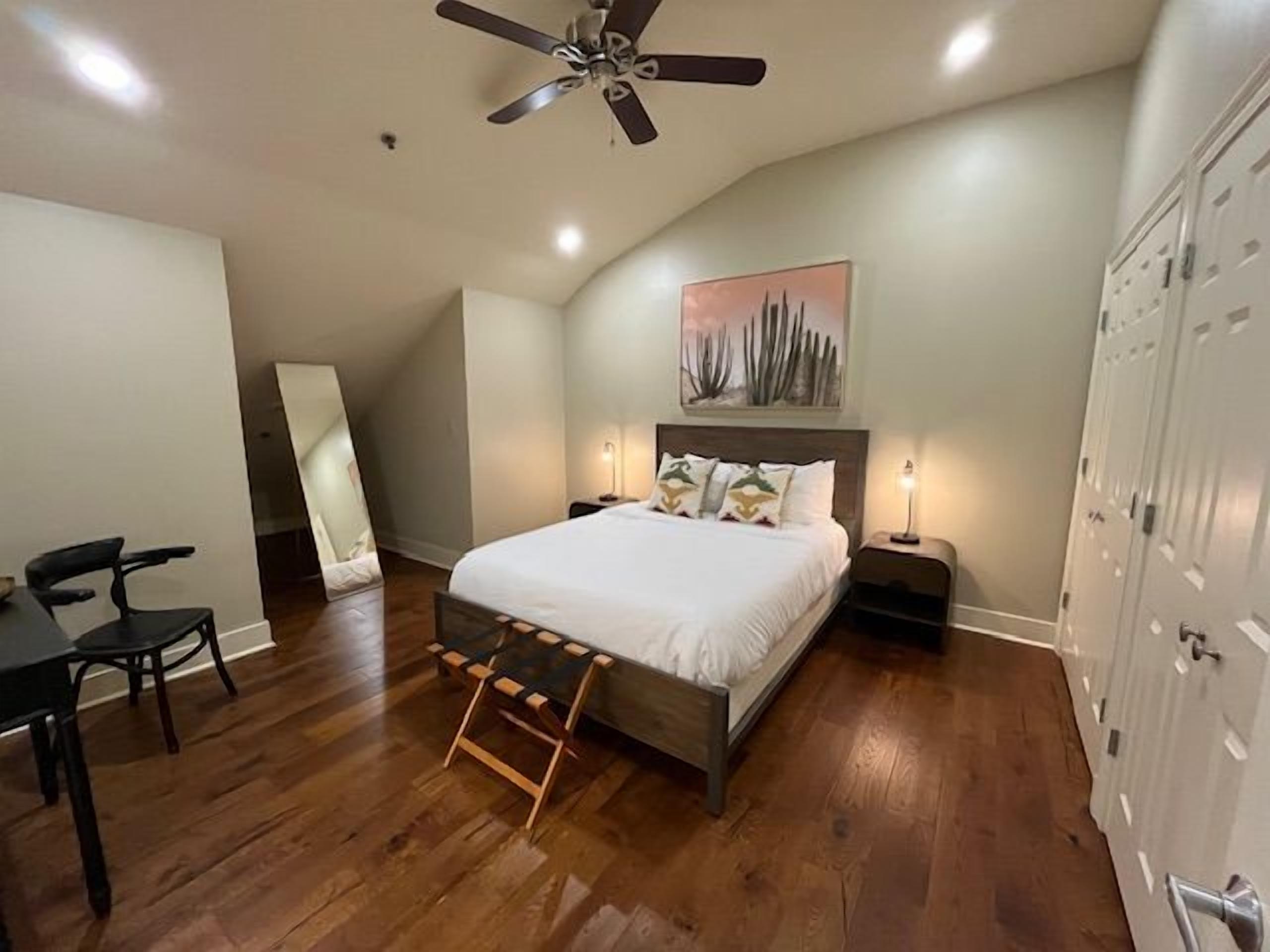 A bedroom with a bed, bedside tables, a ceiling fan, a large mirror, and a wardrobe.