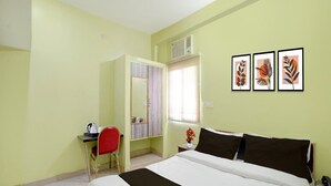 Hotelkamer met een bed, een bureau met stoel, een kledingkast, een raam met jaloezieën en drie ingelijste foto's aan de muur.