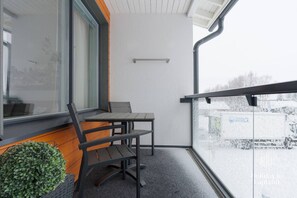 Ein Balkon mit Tisch und Stühlen, einer Topfpflanze und Blick auf eine verschneite Landschaft.