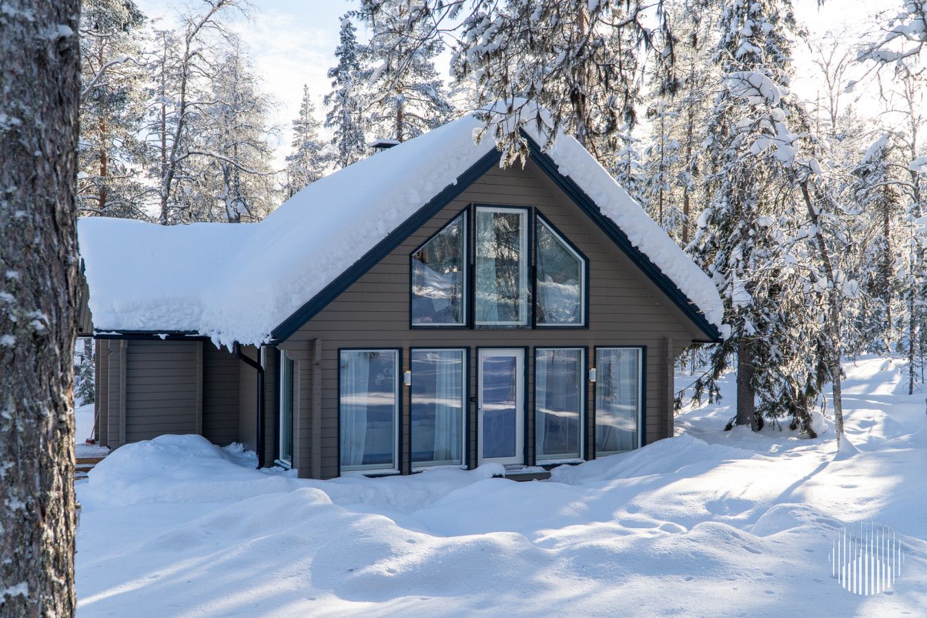 A cabin with a large window, surrounded by snow-covered trees.