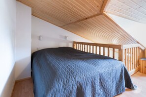 A bedroom with a wooden ceiling, a bed with a quilted cover, and a wooden railing. - Postintie 1608 by Holiday in Lapland (Levi)