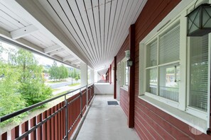 A covered outdoor corridor with a concrete floor, metal railing, and large windows with blinds. - Postintie 1608 by Holiday in Lapland (Levi)
