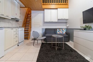 A compact kitchen with white cabinets, a grey sofa, and a small round table. - Postintie 1608 by Holiday in Lapland (Levi)