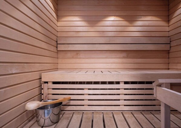 Una sauna de madera con bancos y un cubo de metal.