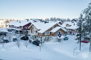 Un edificio innevato con un negozio di articoli da sci e servizio di noleggio, circondato da auto parcheggiate e alberi.