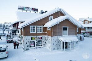 Ein Holzgebäude mit einem Skiverleih und entsprechenden Schildern, umgeben von schneebedeckten Straßen und geparkten Autos.