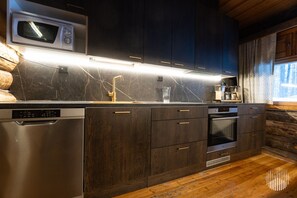 Eine moderne Küche mit dunklen Holfschränken, einem Edelstahl-Geschirrspüler, einer Mikrowelle und einem Backofen.