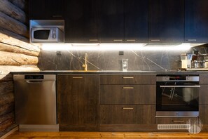 A modern kitchen with dark wood cabinets, stainless steel appliances, and a marble backsplash. - Ukonlammentie by Holiday in Lapland (Ruka)