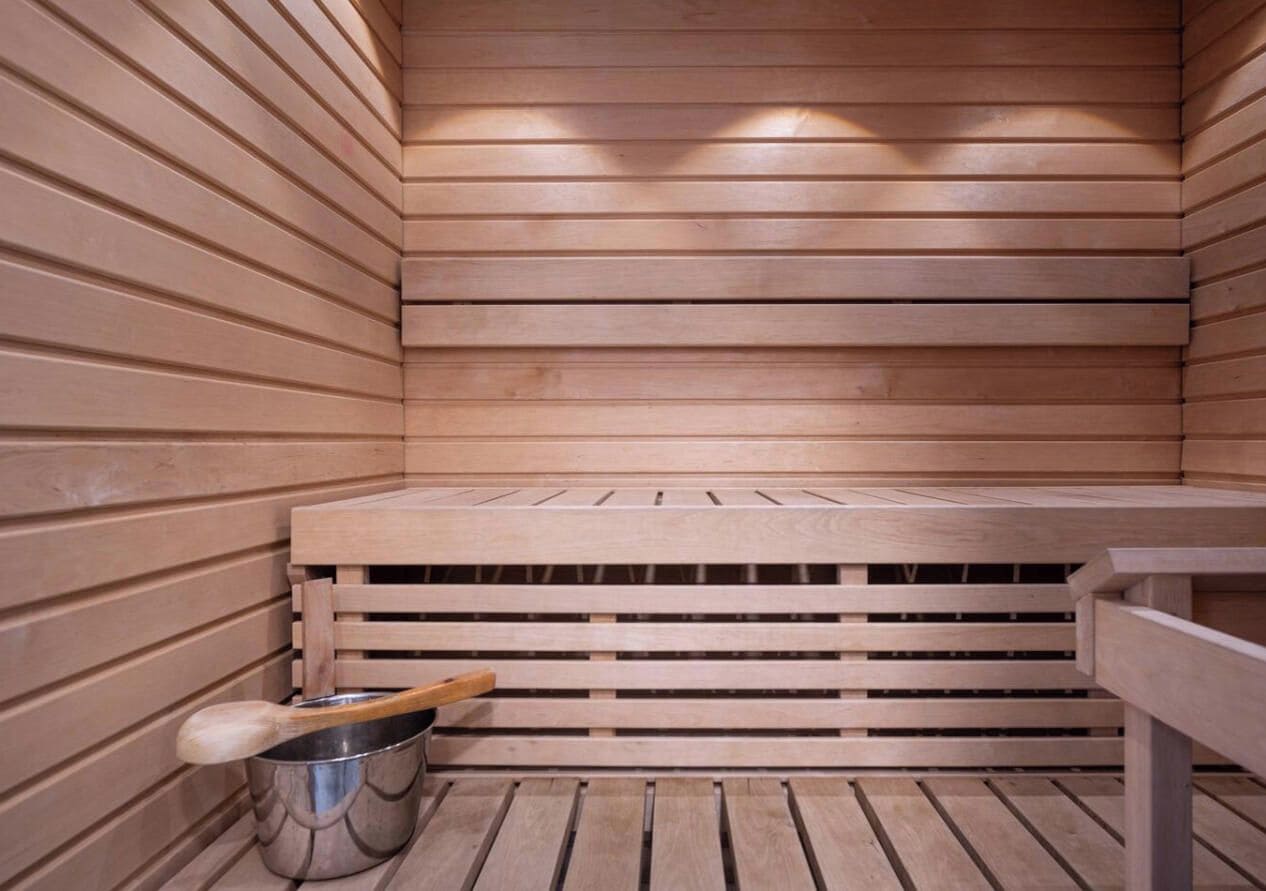 A sauna with wooden benches and a metal bucket with a wooden handle.