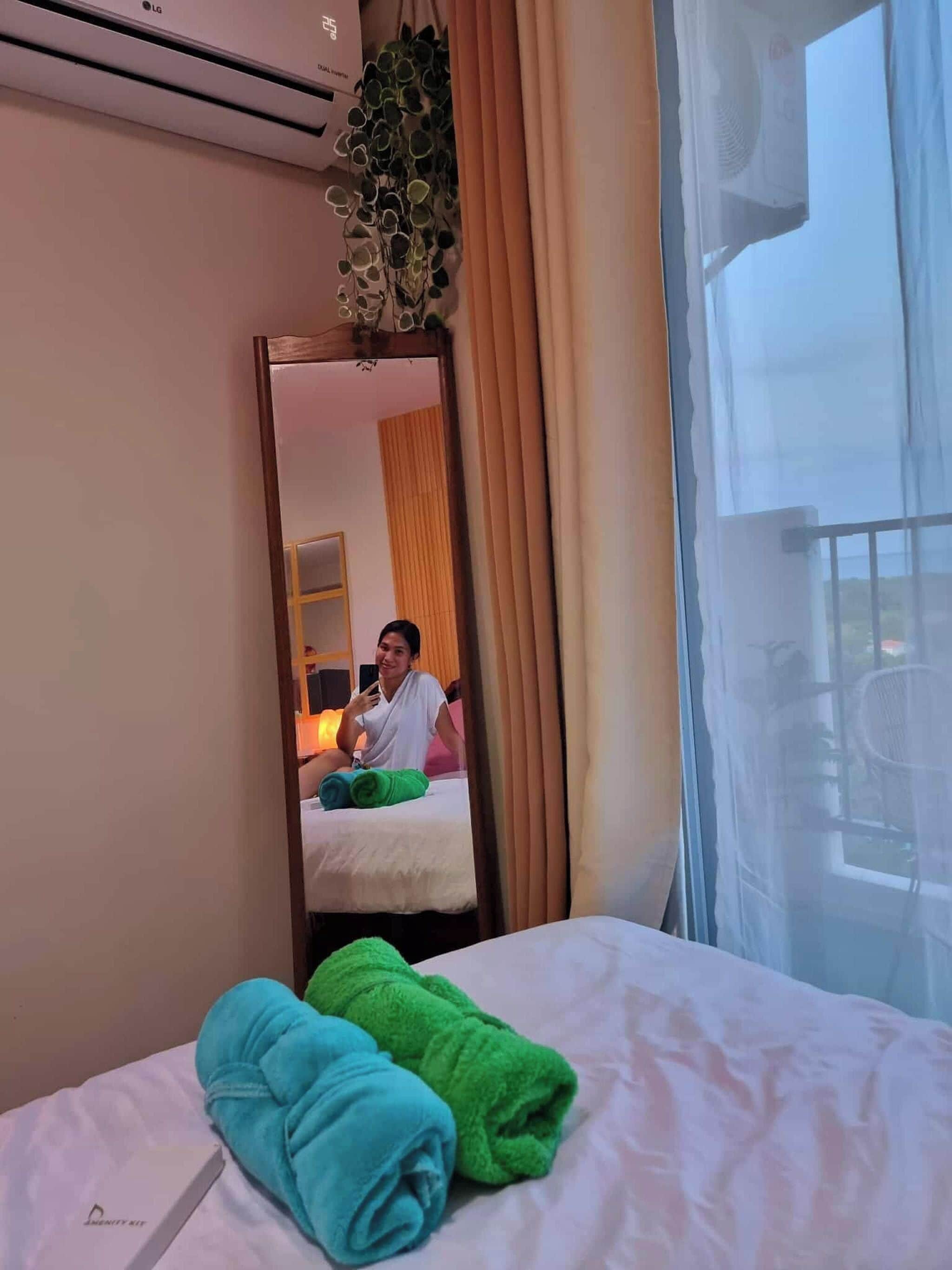 Una habitación de hotel con una cama, un espejo, una ventana con cortinas y una planta.
