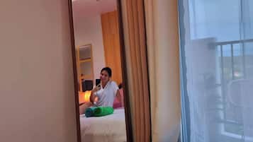 Una habitación de hotel con una cama, un espejo, una ventana con cortinas y una planta.