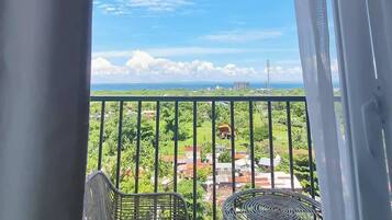 A balcony with two wicker chairs, a view of a green landscape, and a clear sky.
